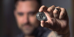 a man holding and showing a silver bitcoin on his left hand