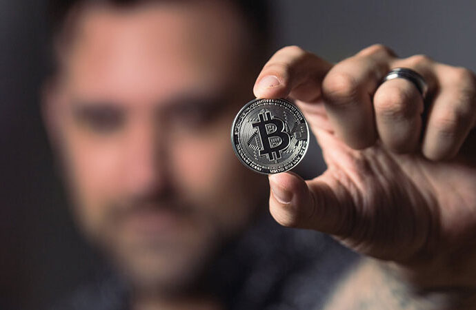 a man holding and showing a silver bitcoin on his left hand